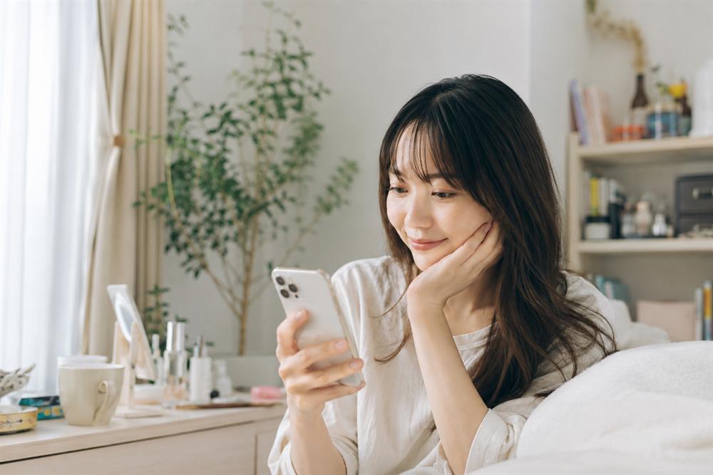 部屋でスマートフォンを見ながら、これからのお金について考えている女性
